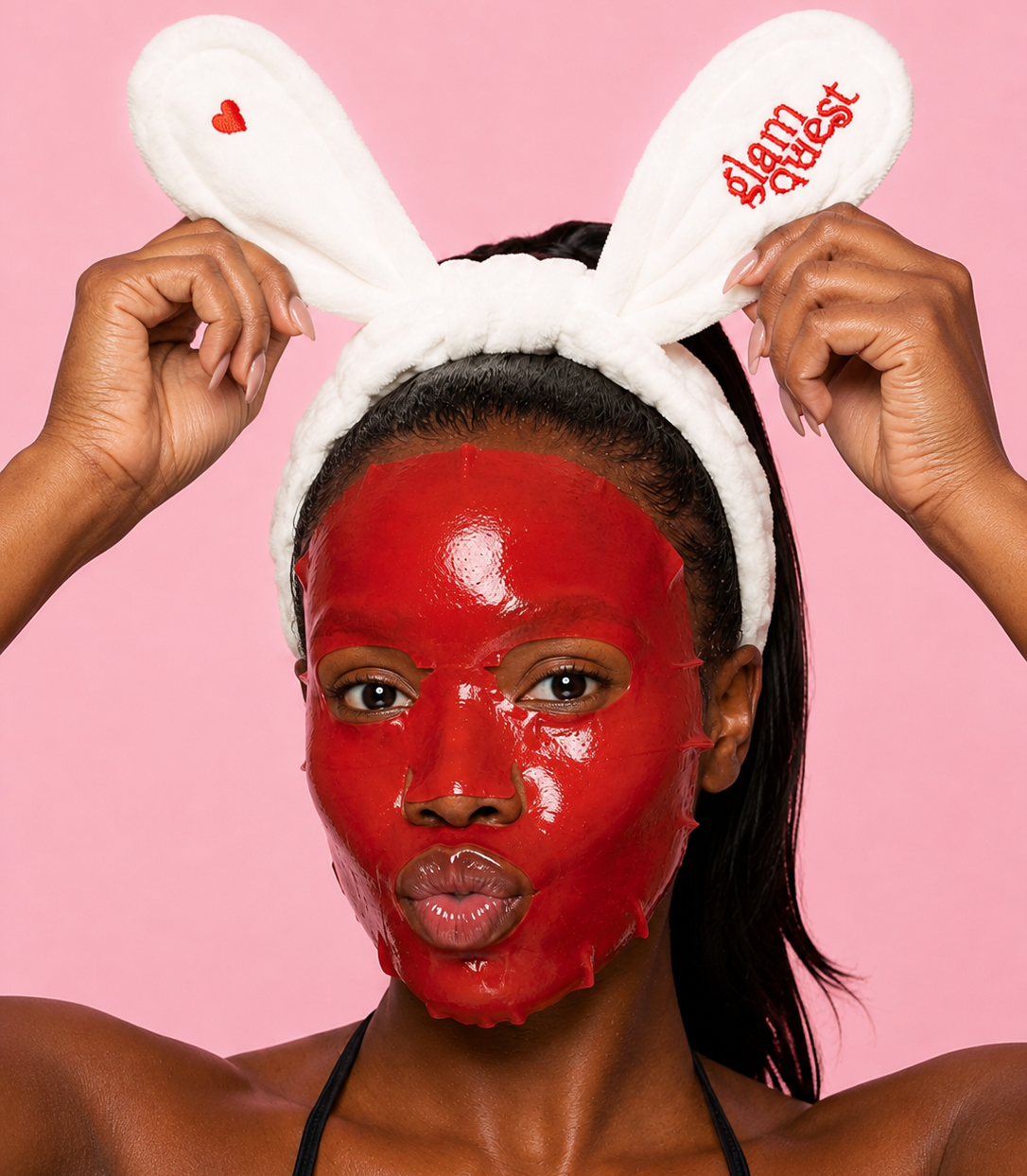 A woman with a glossy red face mask wears a white bunny headband with red embroidered text reading 'slam queen' against a solid pink background.