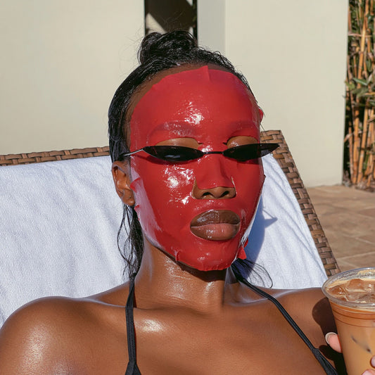Woman with melanin-rich skin relaxing outdoors in the sun wearing a Glamquest Korean skincare hydrogel mask