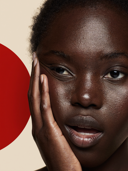 Woman with melanin-rich skin gently touching her clear, glowing cheek, representing the results of a Korean skincare routine